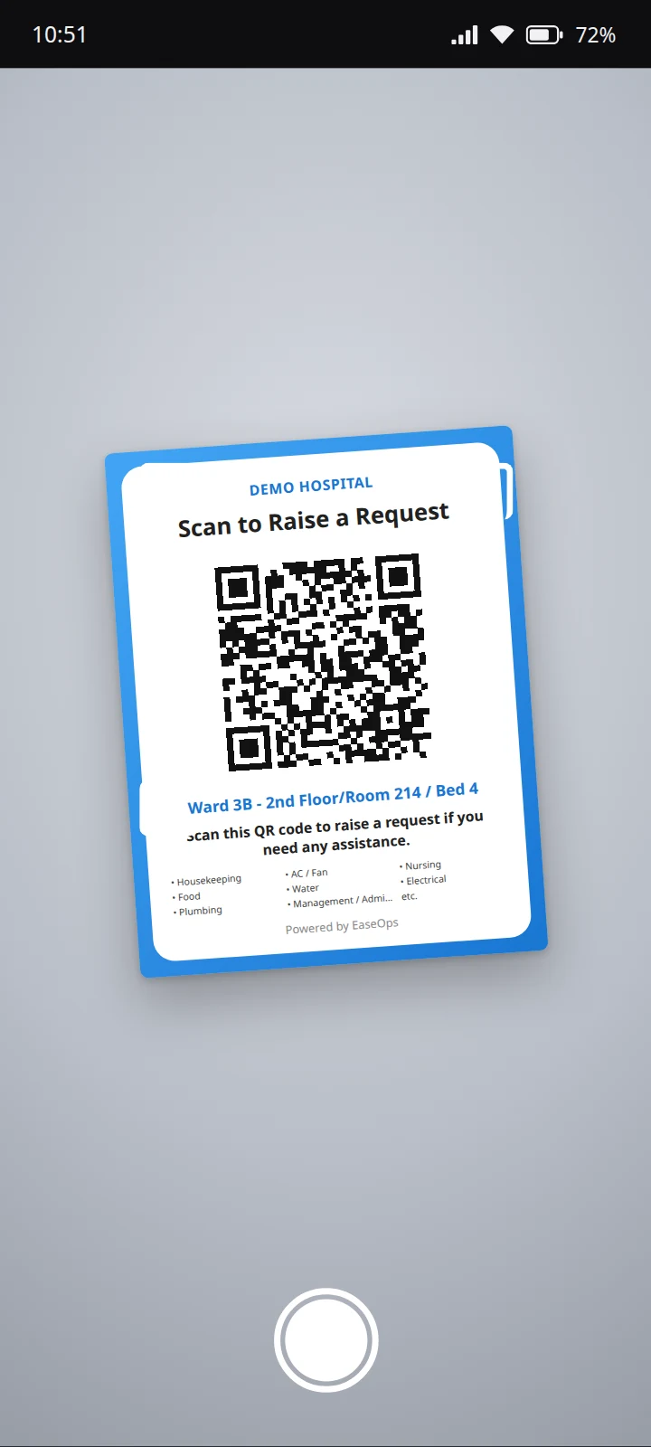 A phone camera pointed at the bedside poster: “Scan to Raise a Request”, a QR code, the ward, room and bed it belongs to, and the request types it takes. Sample data.